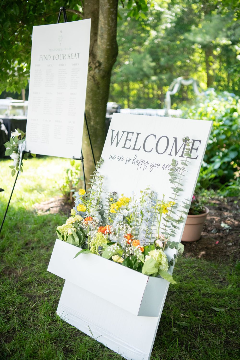 Wedding welcome signs and seating charts arranged in garden setting.