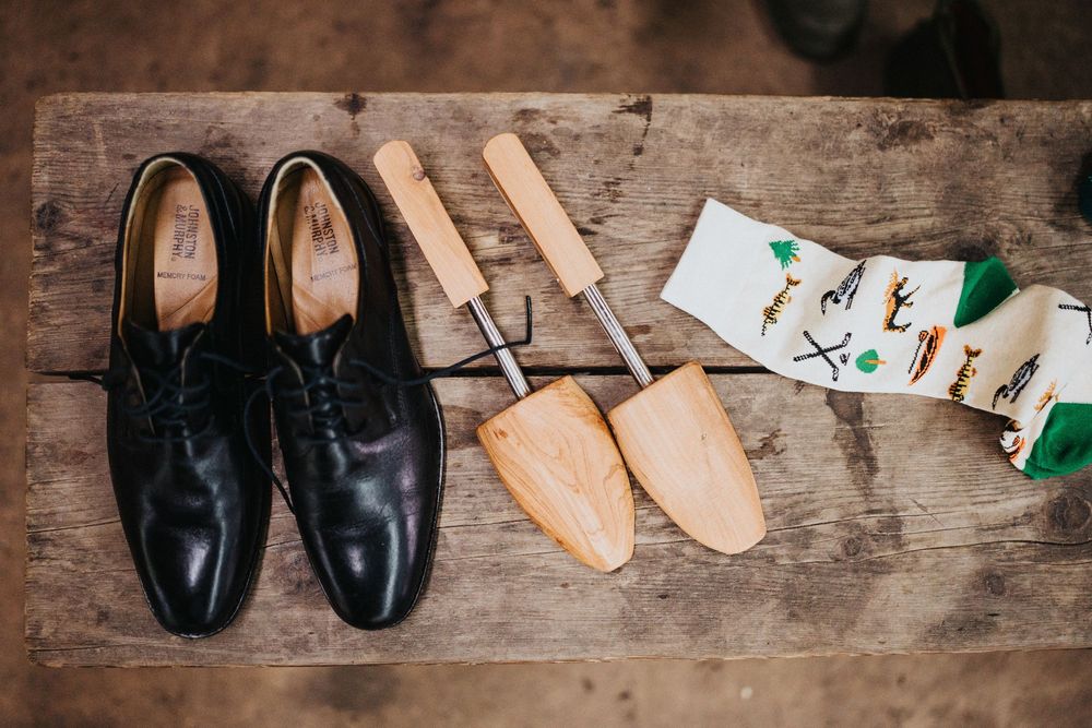 Various leather shoes and wooden shoe forms arranged in a row on a rustic wooden workbench.