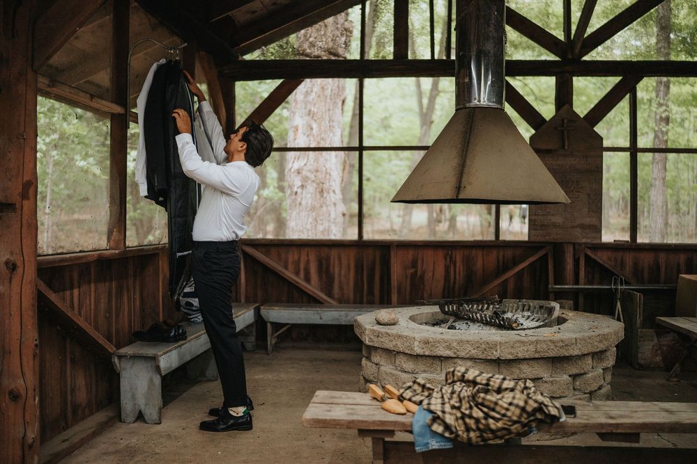 Interior view of a rustic wooden building with a central stone fireplace and natural light streaming through windows.