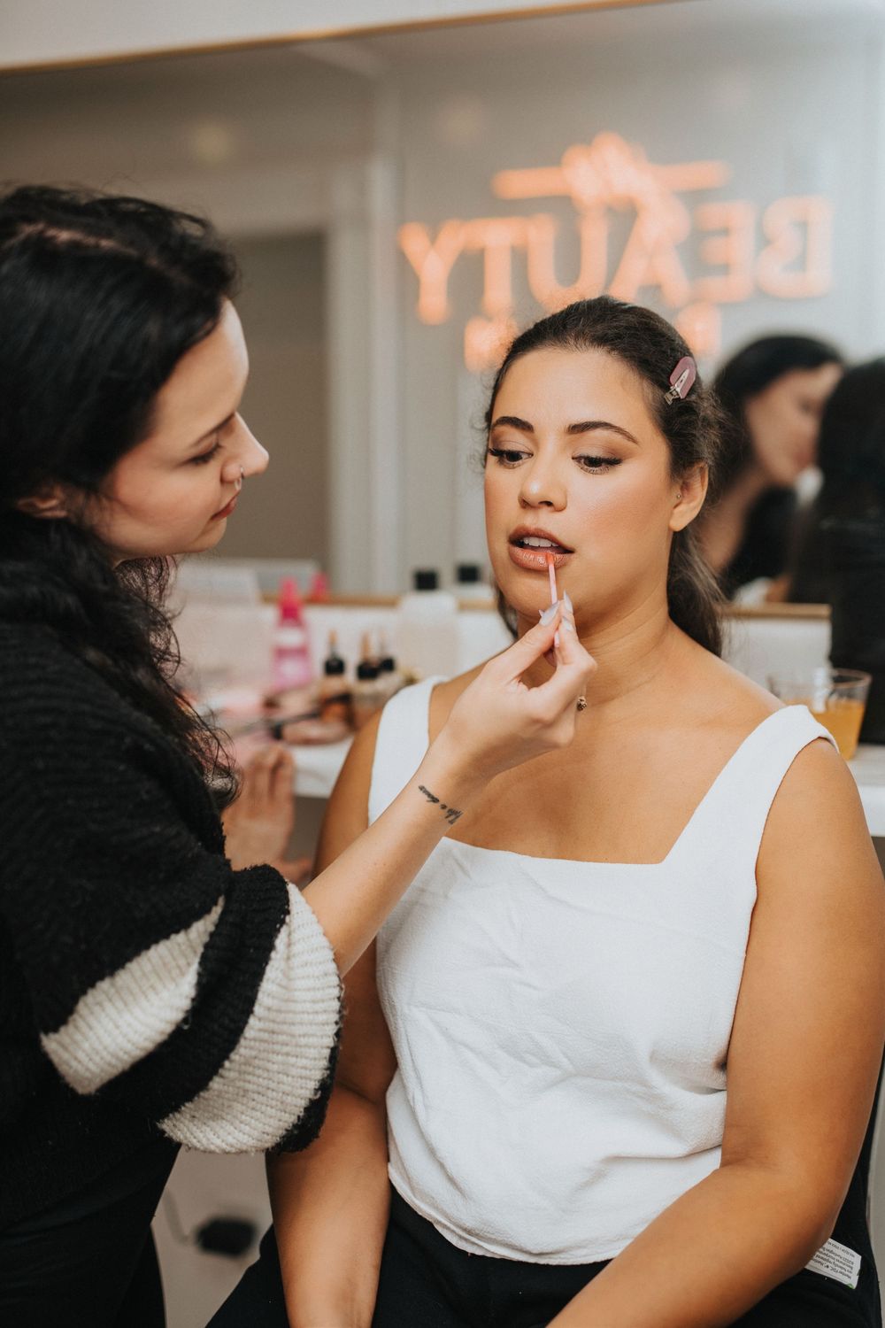 Professional makeup artist applying cosmetics on a client wearing a white top during a beauty session.