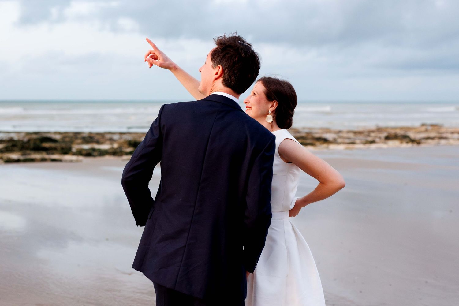 Newlywed couple walking and dancing together on a cloudy beach.