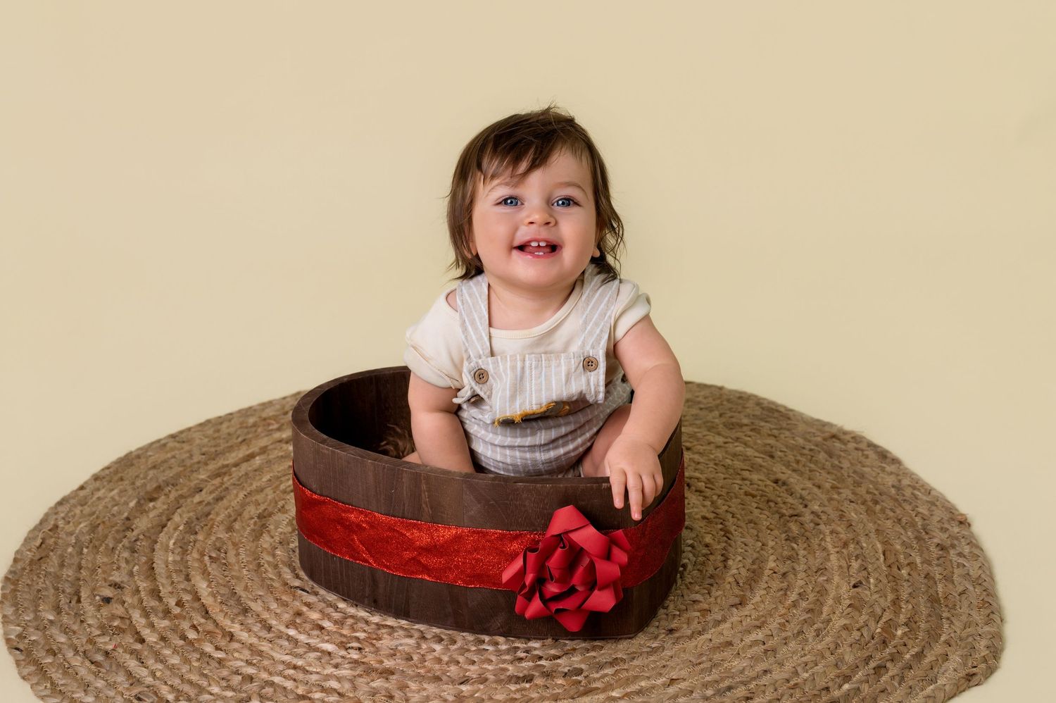 A child in a white dress sits in a large woven straw hat while smiling at the camera.