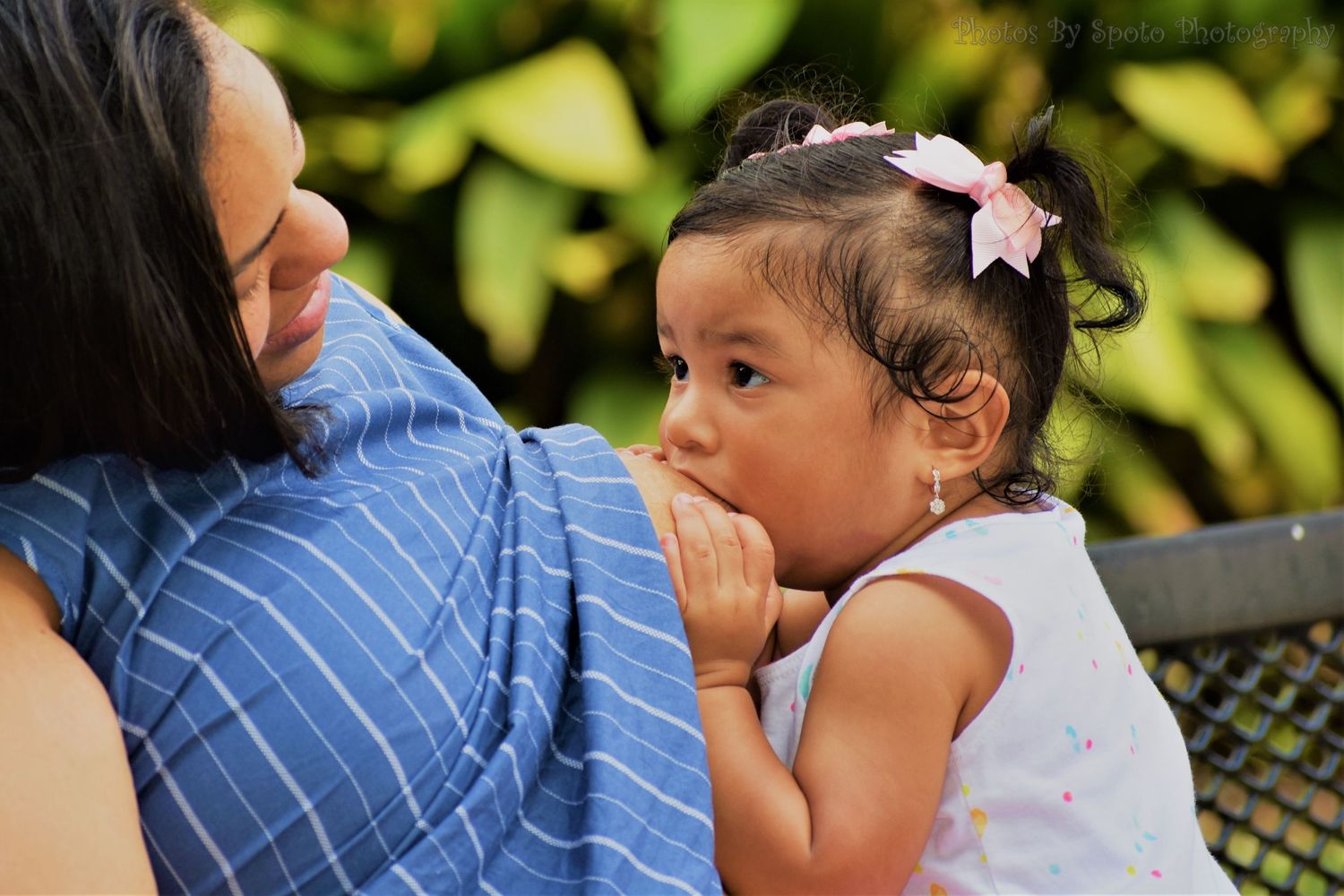 Parent and child share a tender moment outdoors surrounded by green foliage in the background.