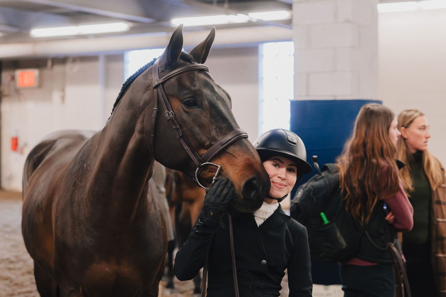 A group of equestrians and horses gather near a stable area during a riding event.