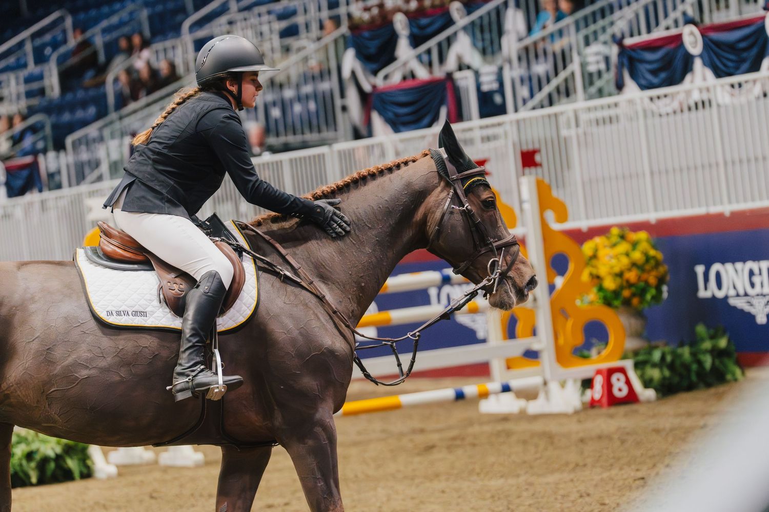 Equestrian rider jumps over a white and orange obstacle during a competitive show jumping event.