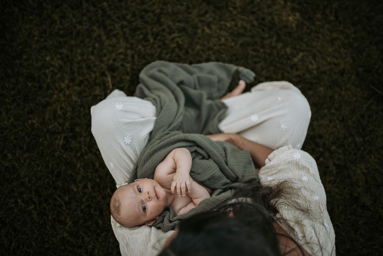 A person lies peacefully on a blanket in the grass wearing a green sweater and white pants.