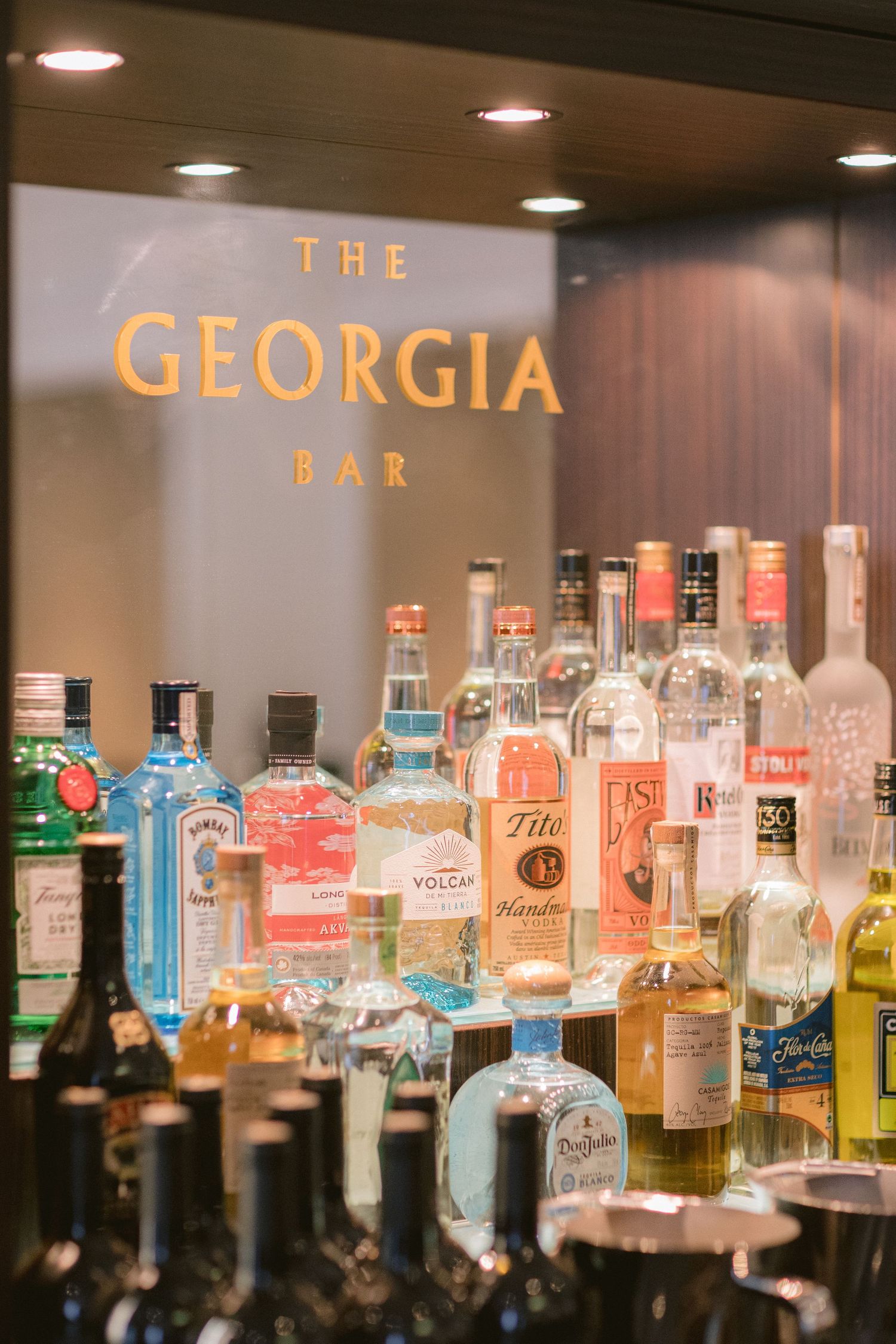Illuminated bar shelves display an extensive collection of liquor bottles with colorful spirits and glowing backlighting.