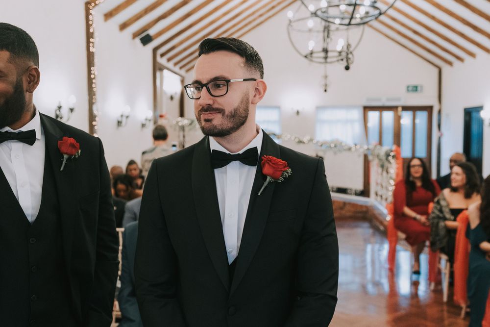 Wedding party members in black tuxedos and red boutonnieres stand together during an elegant indoor celebration.