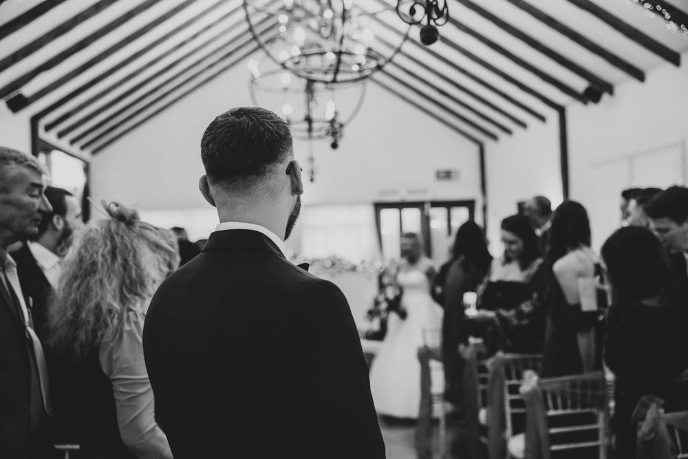 Black and white photo of wedding ceremony attendees seated in rows under wooden beams and chandeliers.