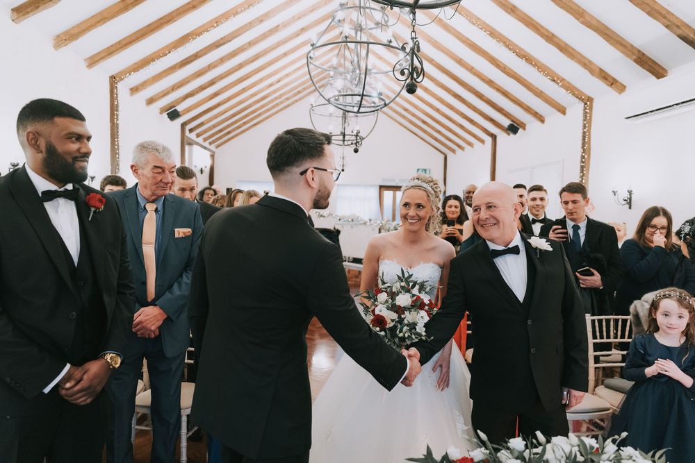 Wedding guests mingle and socialize during an elegant indoor reception with exposed wooden beams and chandeliers.