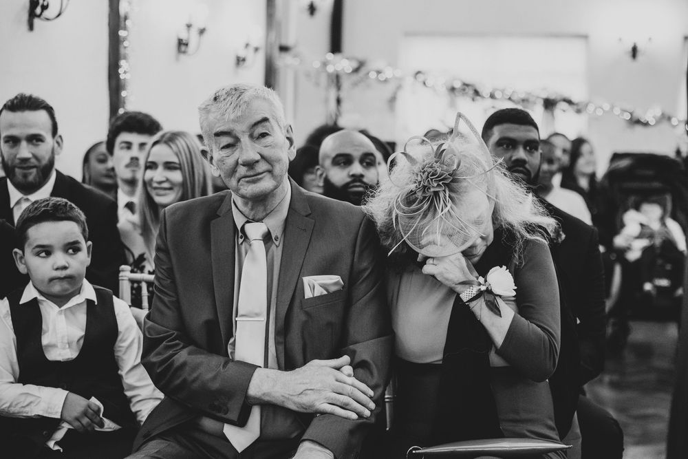 Wedding guests laugh and enjoy themselves during an indoor reception celebration in black and white.