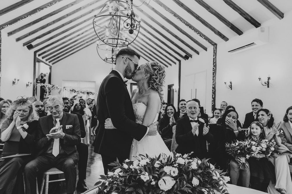 Wedding reception guests mingle and celebrate in a rustic barn venue with exposed wooden beams.