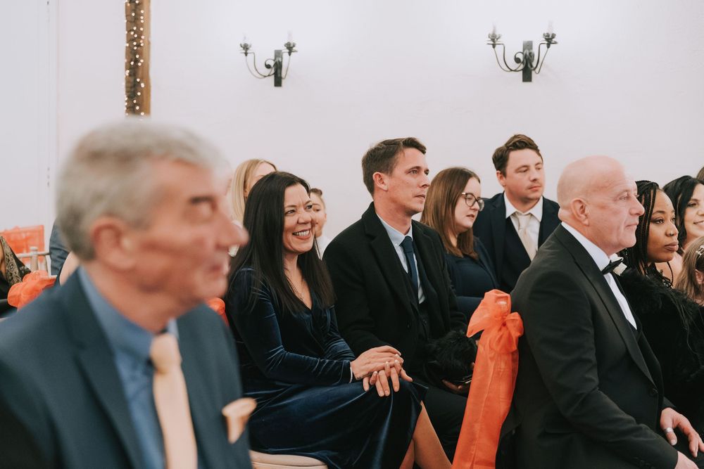 Wedding guests seated in rows at an elegant white indoor venue with natural lighting and modern decor.