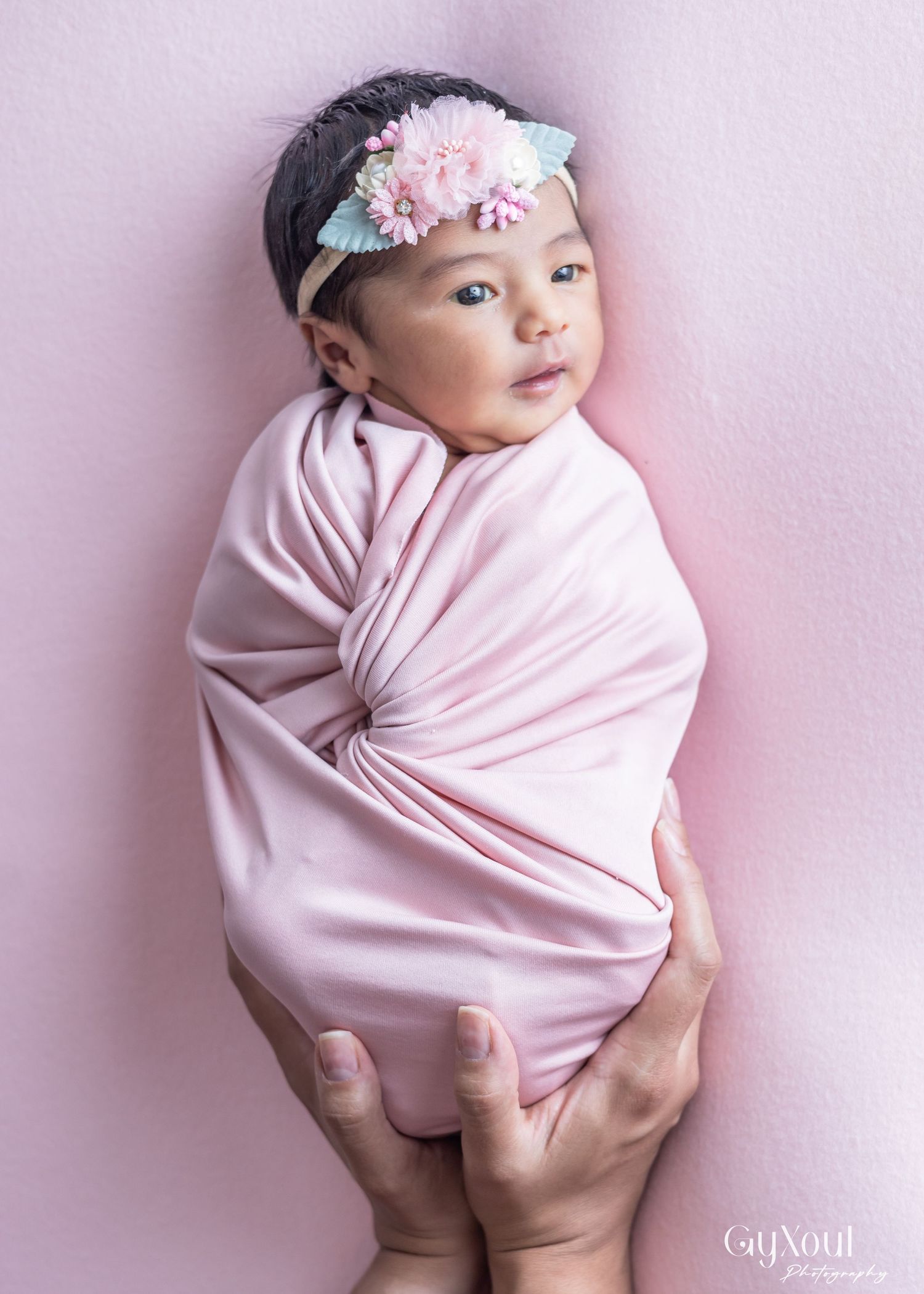 A newborn baby wrapped in pink swaddle with floral headband shown in four different poses against a pink backdrop.