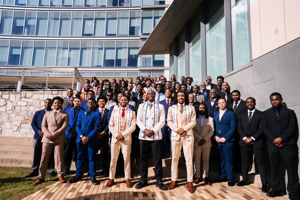 A group of professionally dressed people stand in a line against a building exterior for a formal group photo.