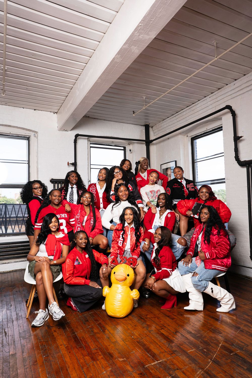 Group of people in red jerseys and casual wear posing together on hardwood floor in bright indoor space.