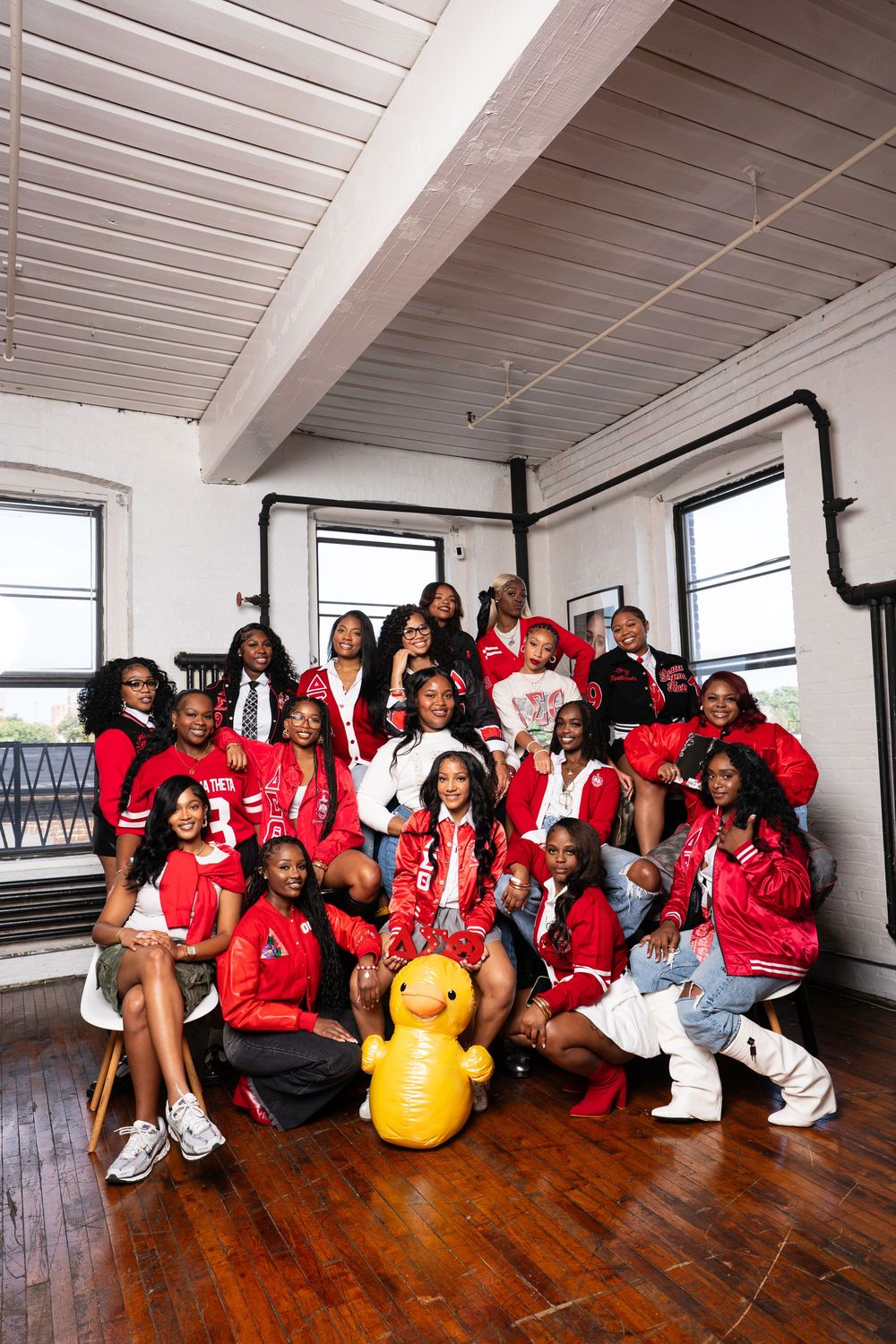 A group in matching red shirts sits together on a wooden floor in a bright studio space.