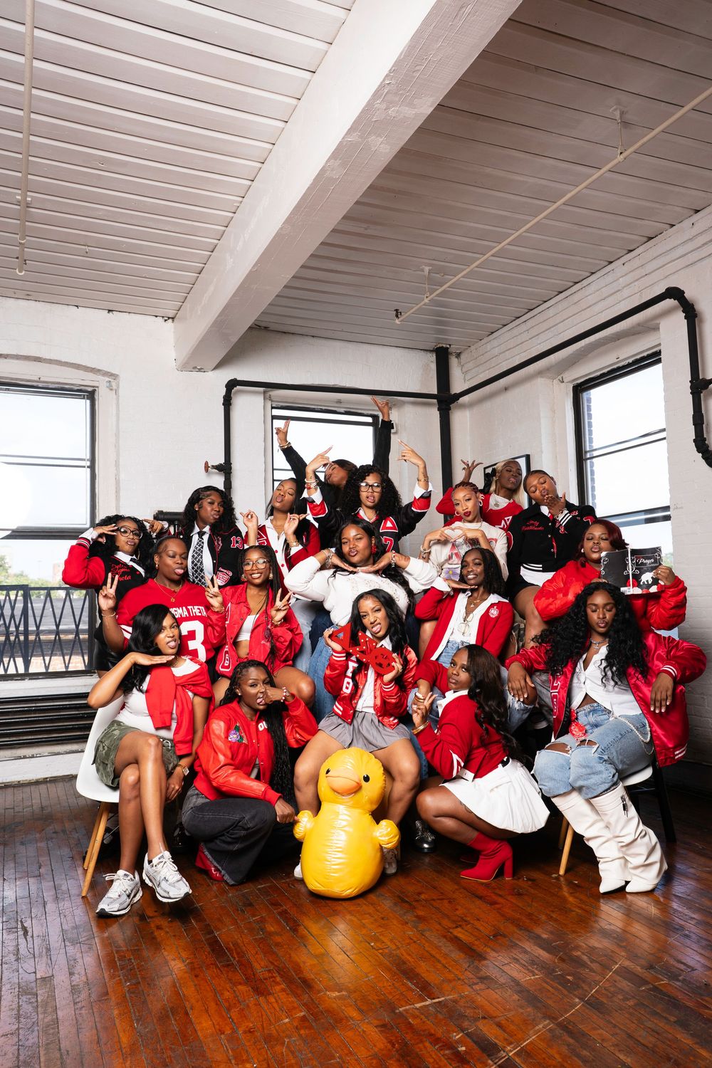 Large group wearing red and white outfits poses together on wooden floor in bright indoor space.
