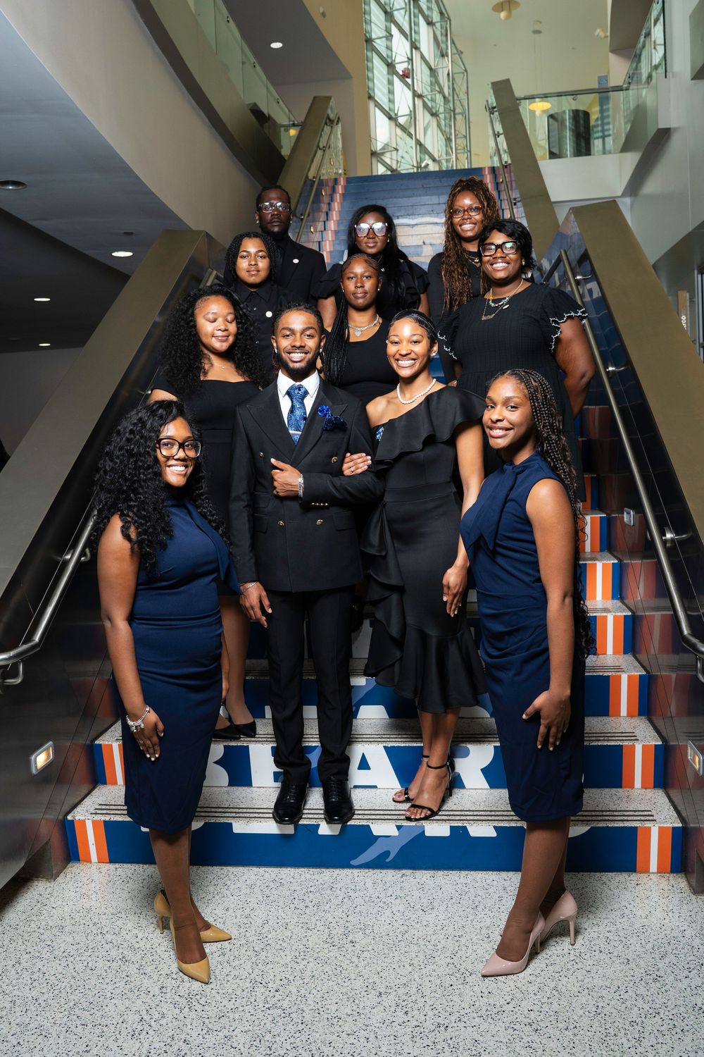 A group in formal navy blue and black attire poses together on stairs for a special occasion photo.