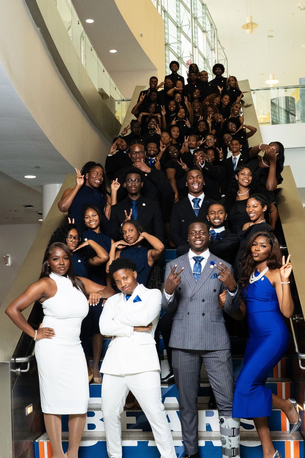 A group of formally dressed people pose together on stairs in coordinated blue, white and gray outfits.