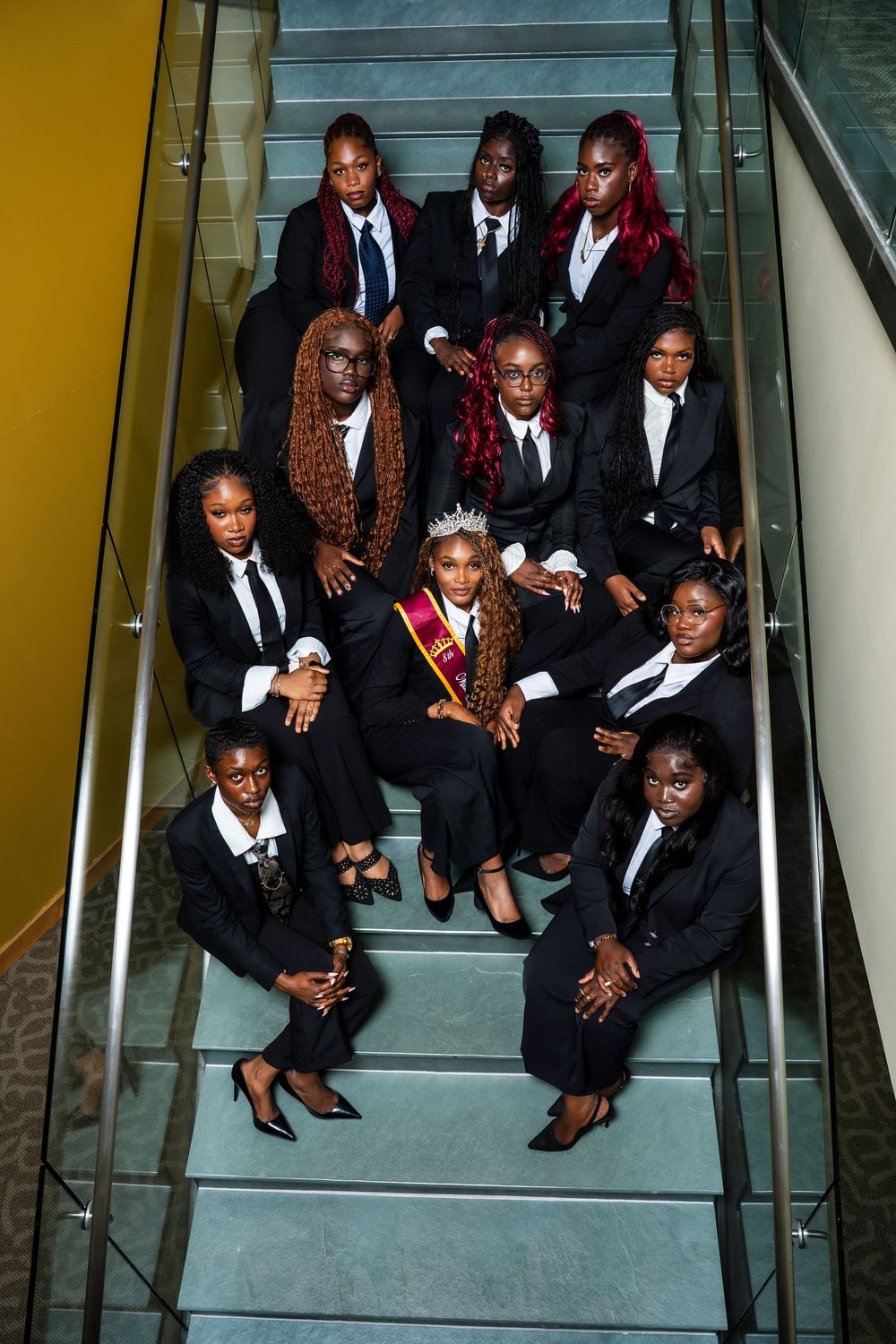 A group of formally dressed people in black attire sitting together on modern concrete stairs.