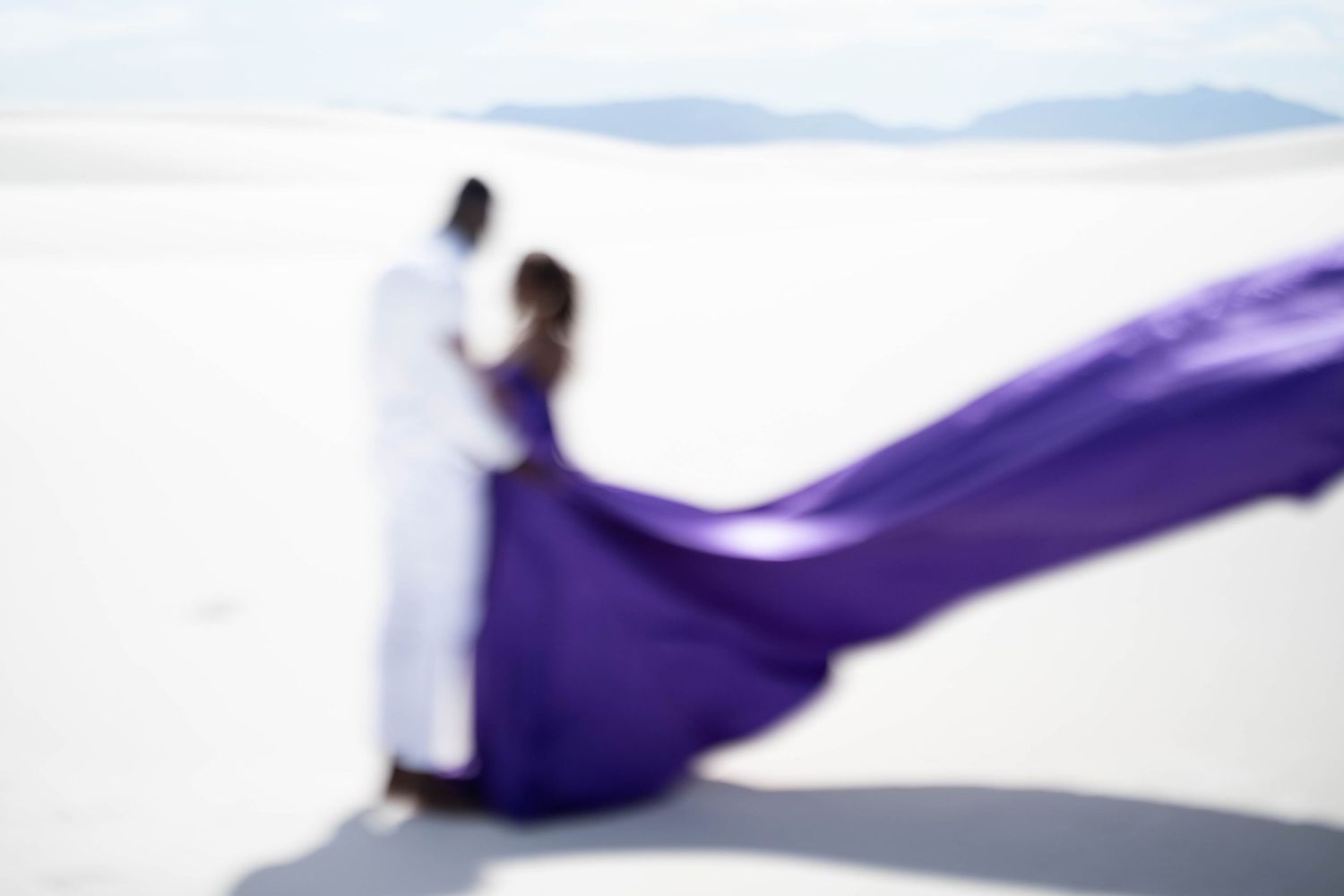 A flowing purple fabric creates graceful curves and waves against a white background in an artistic composition.