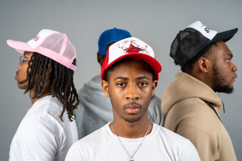Group of people wearing baseball caps and casual clothing posing against gray background.