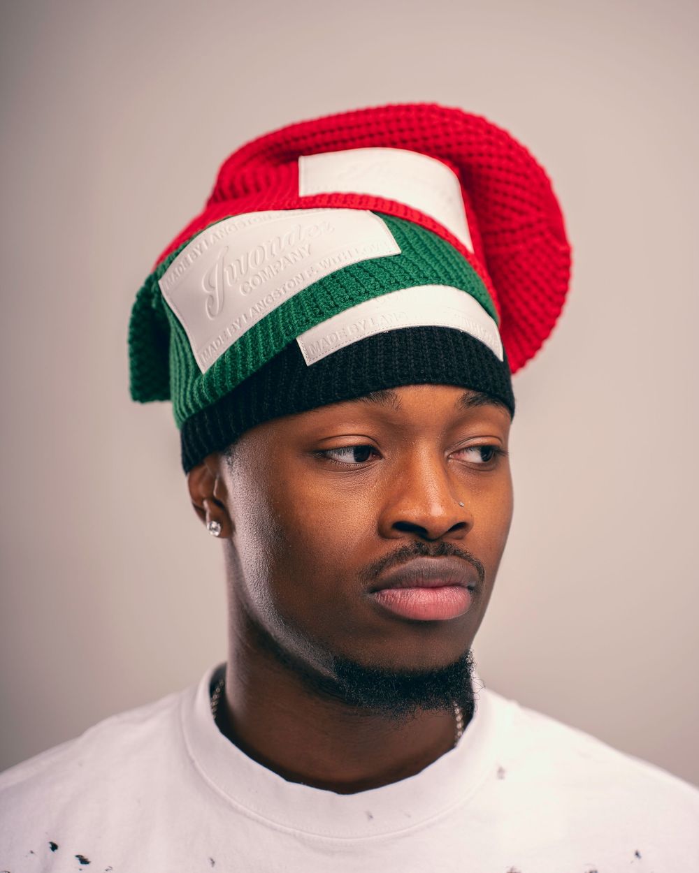 Person wearing a red and green striped winter beanie hat poses for a series of close-up portraits against a light background.