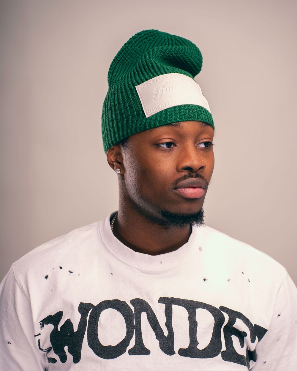 Person wearing a green knit beanie and white sweatshirt with 'WONDER' text in studio lighting.