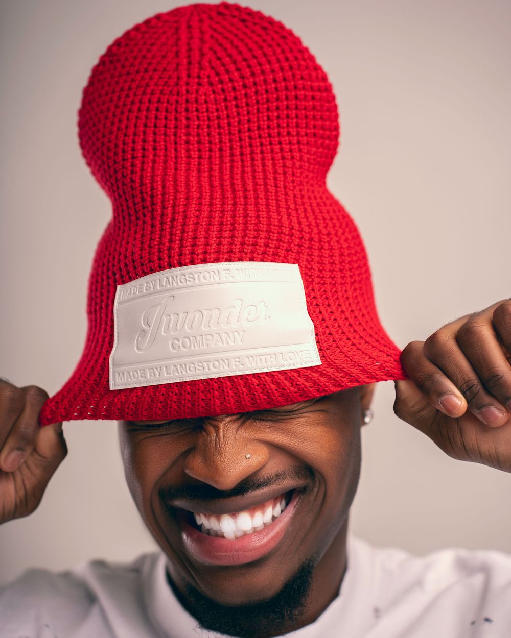 A sequence showing a bright red knit beanie with a white label being adjusted and worn at different angles.