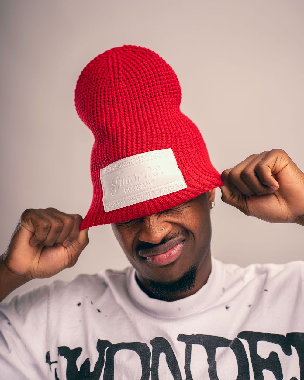 A person wearing a bright red knit beanie and white t-shirt poses in a series of playful expressions.