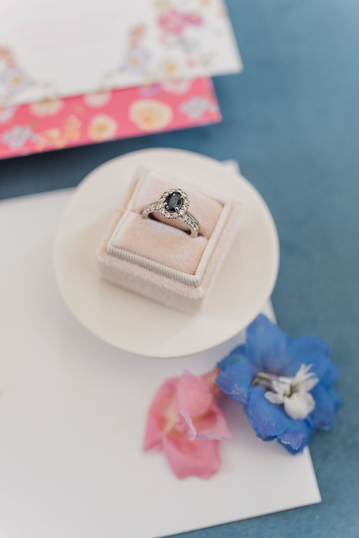 Wedding ring displayed on white paper with pink and blue floral accents.