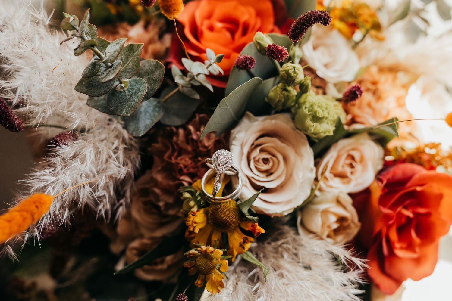 A romantic wedding bouquet featuring coral roses, beige roses, and delicate pampas grass arranged together.