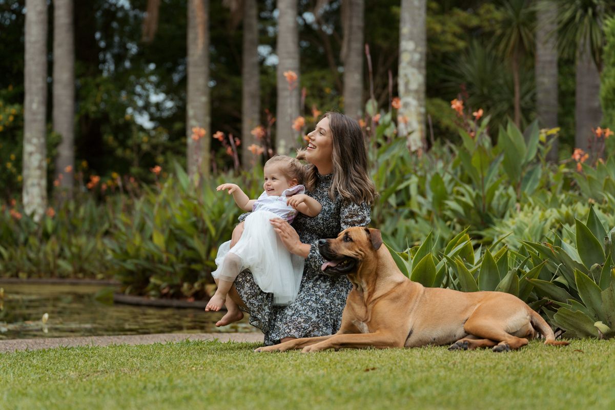 Mom and her daughter and their dog relaxing together on grass in a peaceful garden setting during a photoshoot in sydney Fagan Park