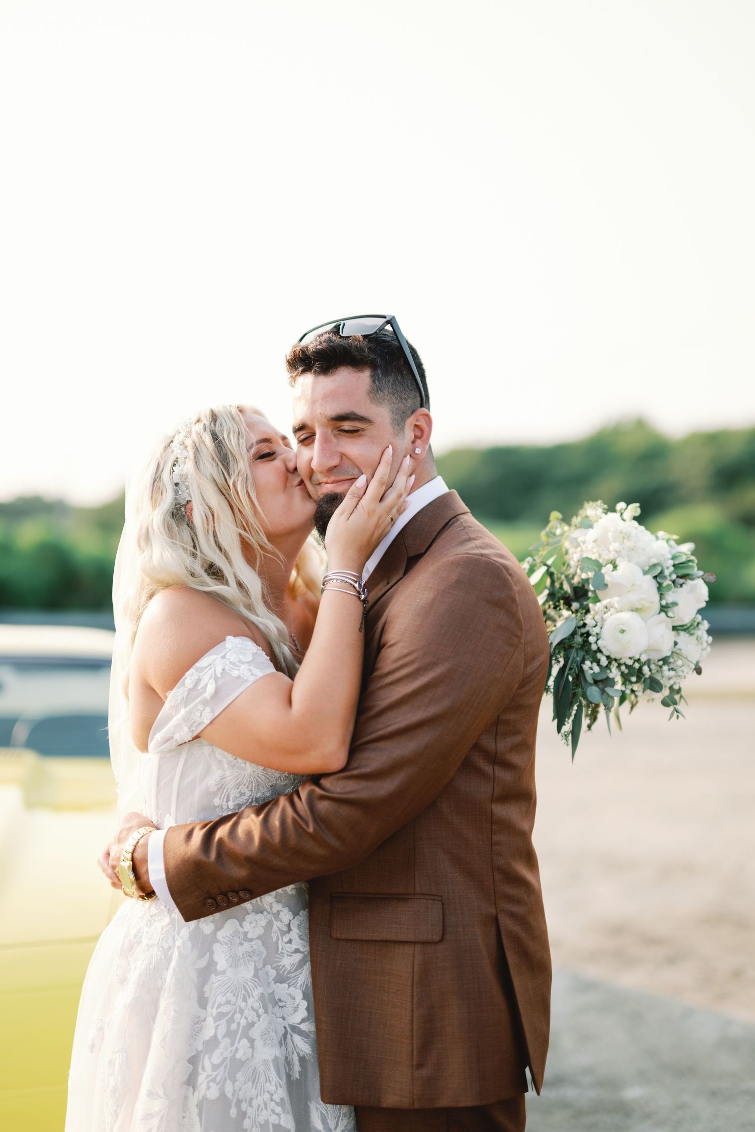Romantic moment between newlyweds outdoors with white floral bouquet.