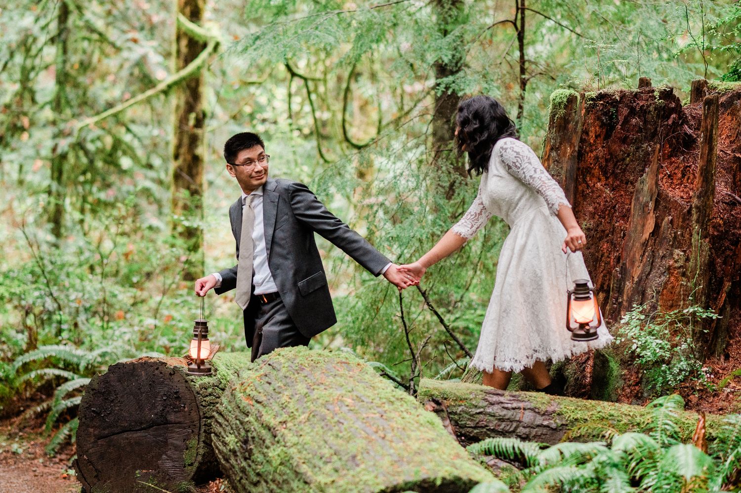 A bride and groom poses in a lush forest setting for wedding photos while holding vintage lanterns