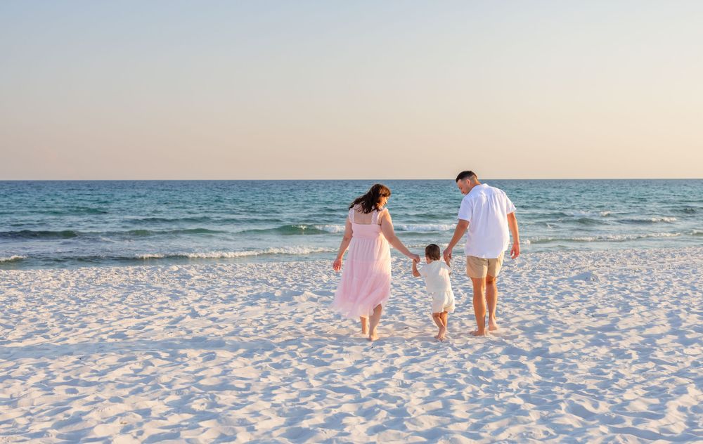 A couple walks hand in hand along a pristine white sand beach at sunset with ocean waves in the background.