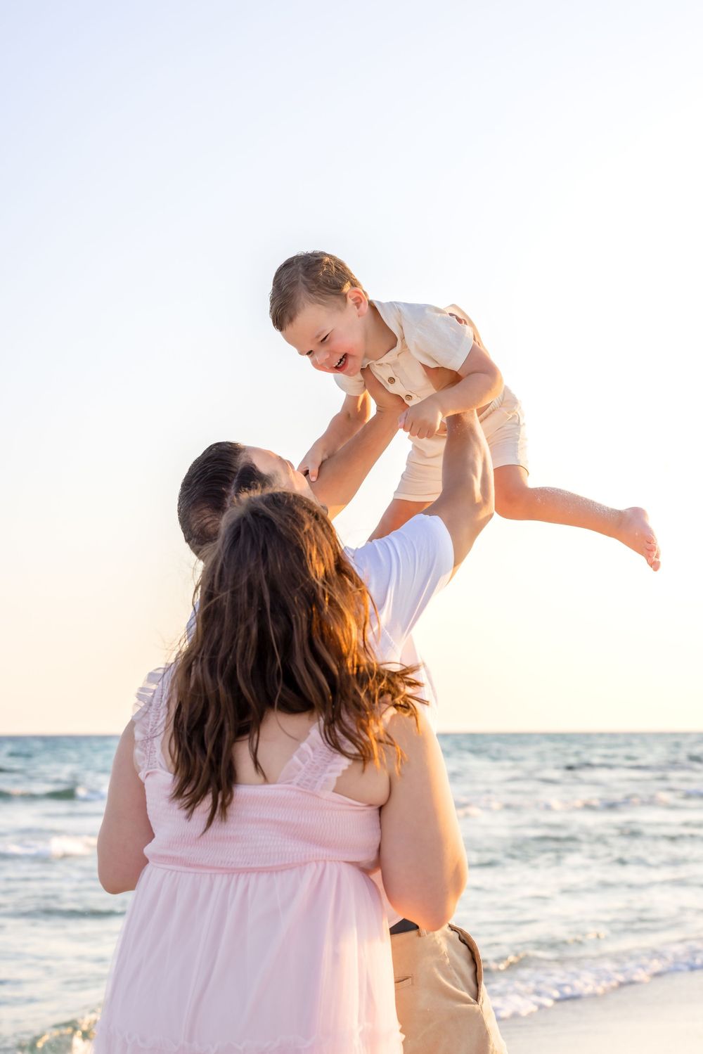 A family plays together on a sunny beach at sunset in matching white and pink outfits.