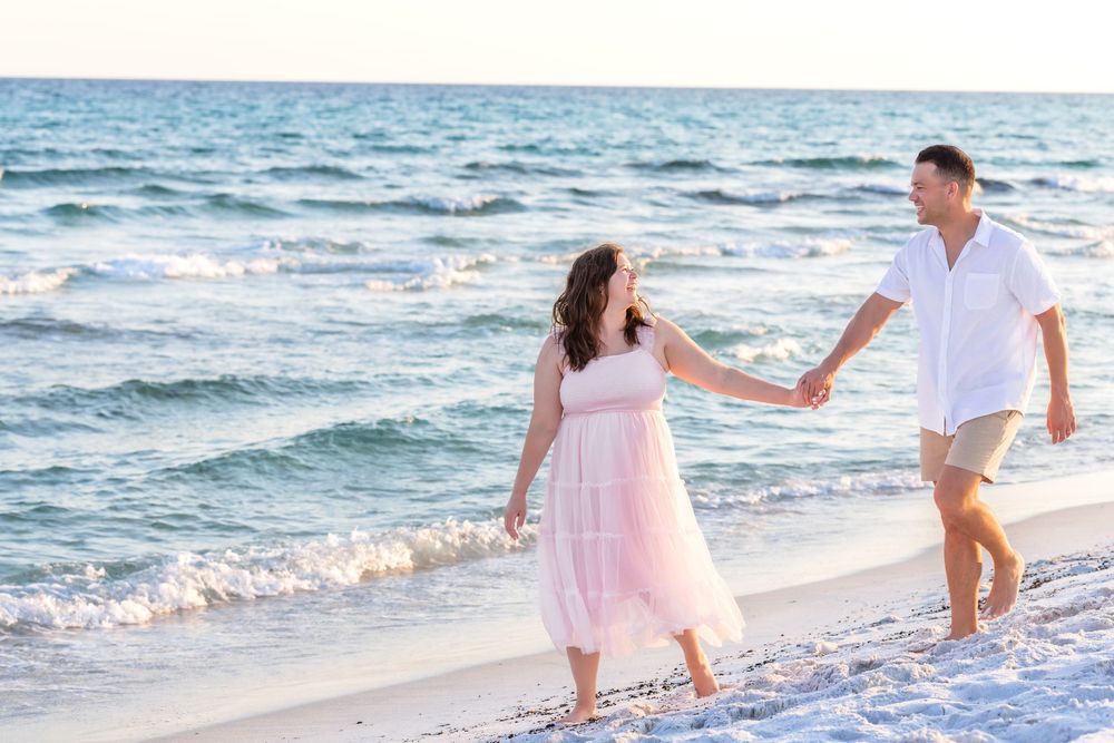 Couple walking hand in hand along a beach shoreline at sunset with waves lapping at their feet.