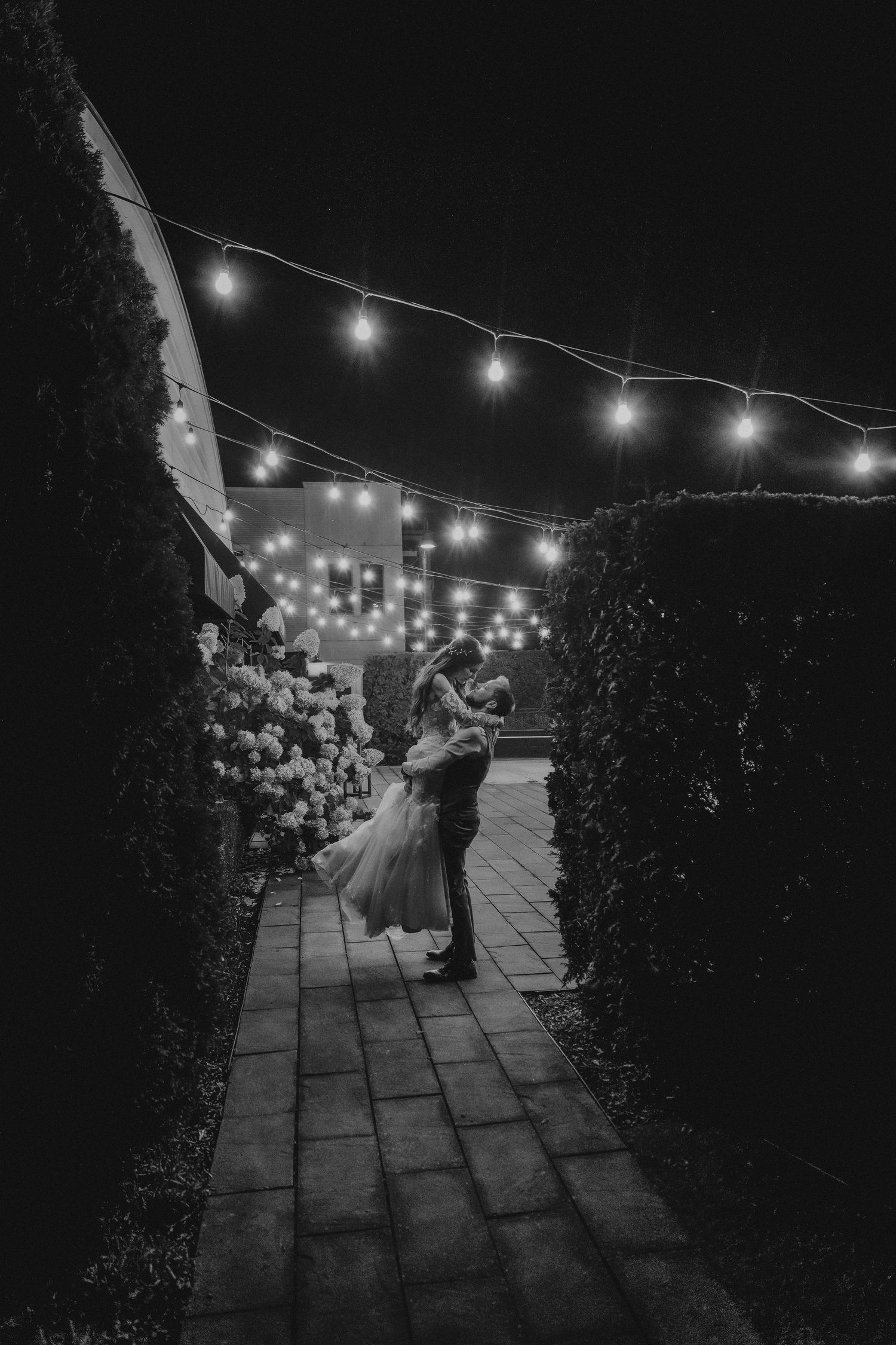 A romantic dance scene under twinkling string lights illuminating a garden pathway at night.