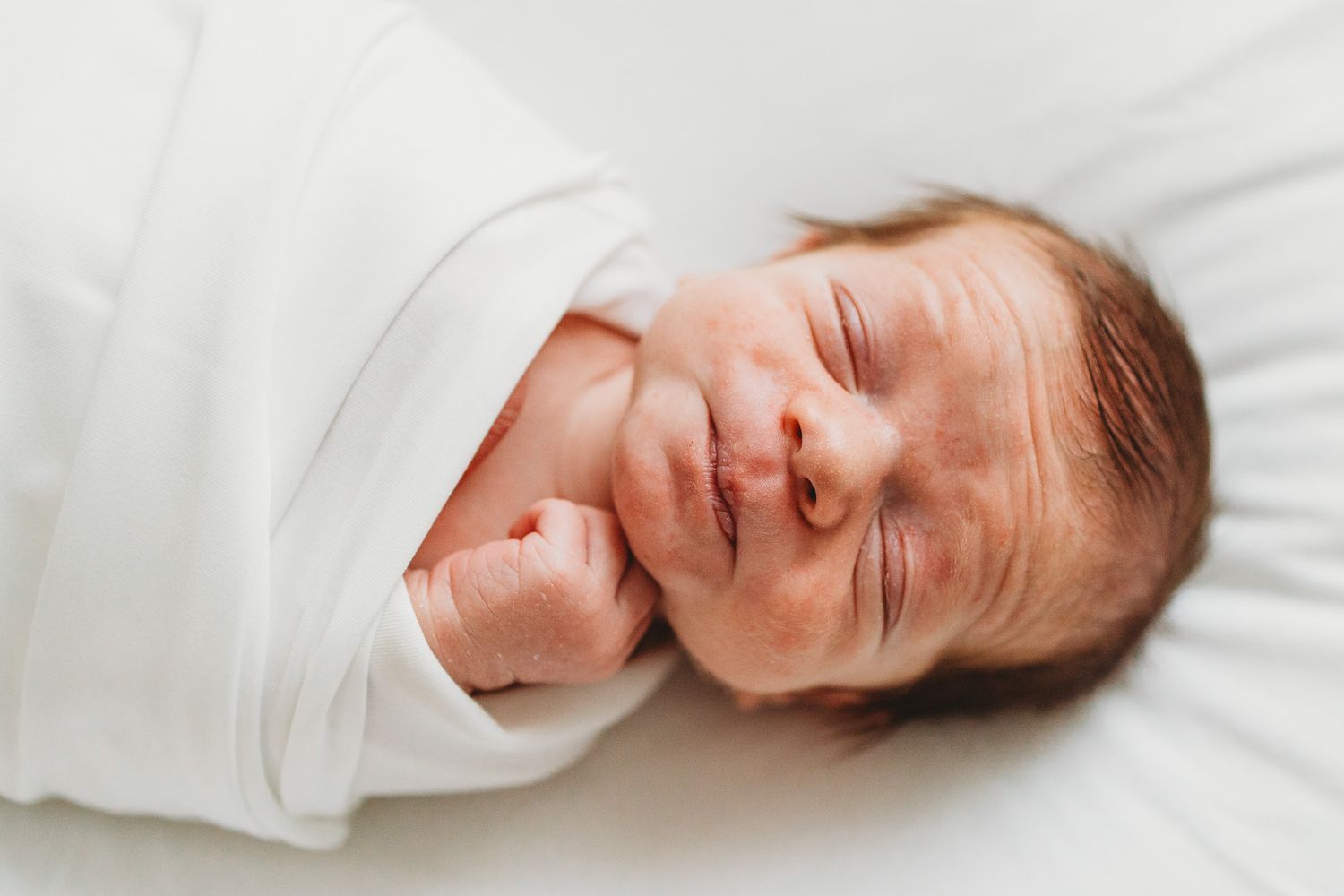 A series of close-up photos showing a sleeping baby wrapped in white blankets from different angles.
