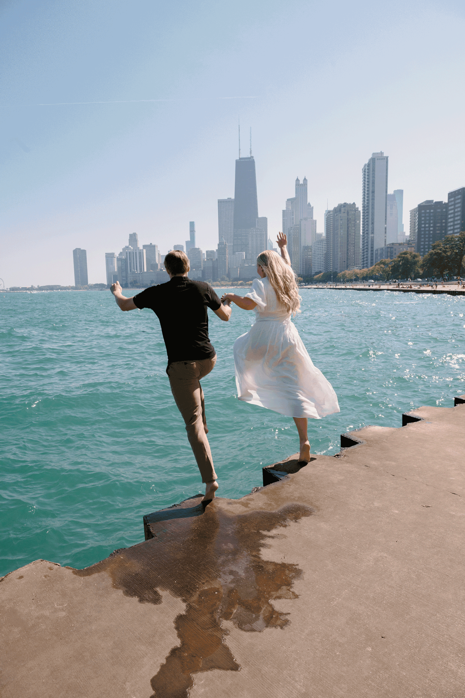 Two figures leap joyfully along Chicago's waterfront with the city skyline and Lake Michigan in the background.