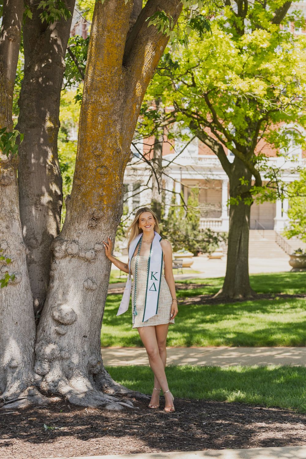 Mizzou senior in Kappa Delta graduation sash poses by a large tree on the University of Missouri campus.