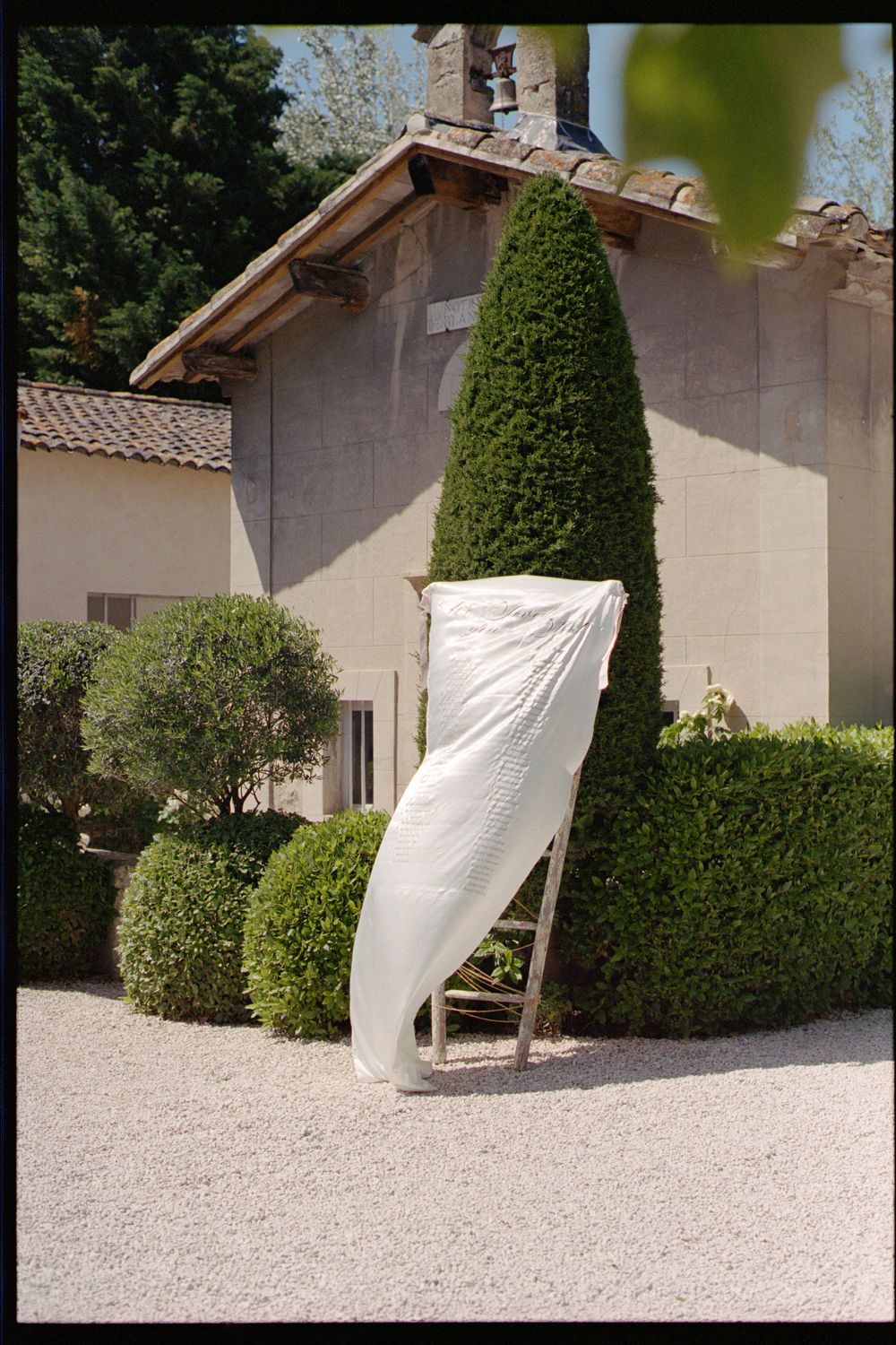 White sheet billowing in the wind against a garden wall with manicured topiary bushes and gravel landscaping.