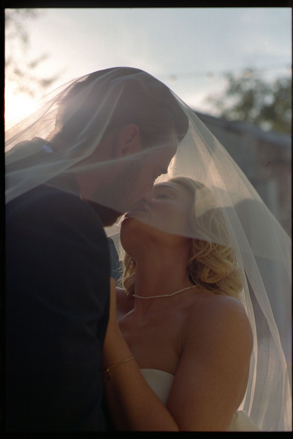 Romantic moment under a delicate white veil during an outdoor wedding ceremony.