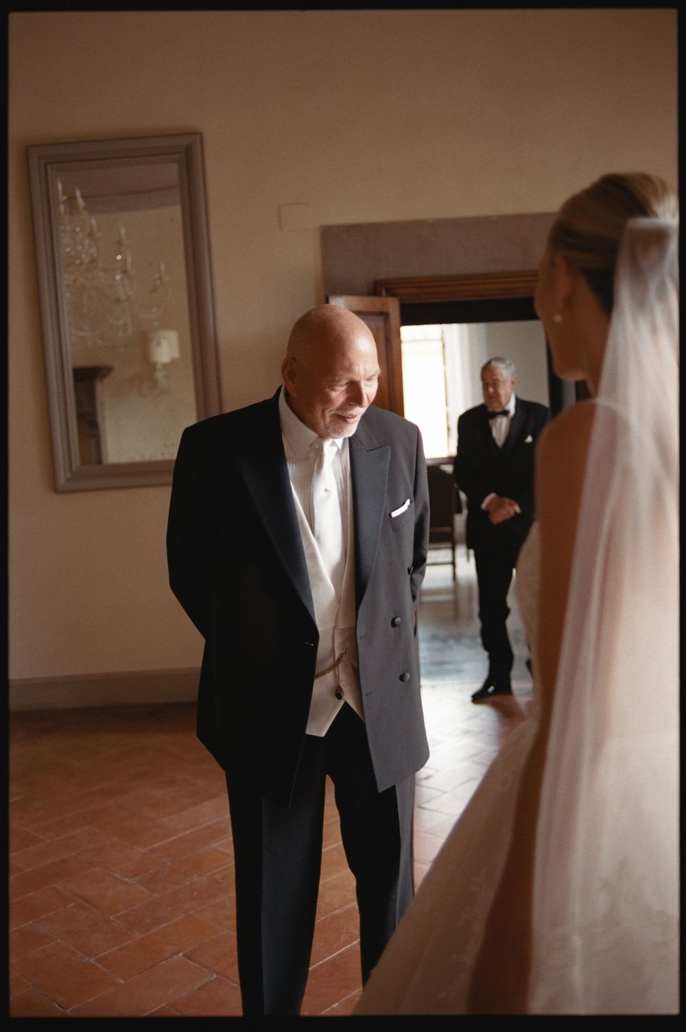 Elderly man in tuxedo shares emotional moment with bride in veil at elegant wedding venue.