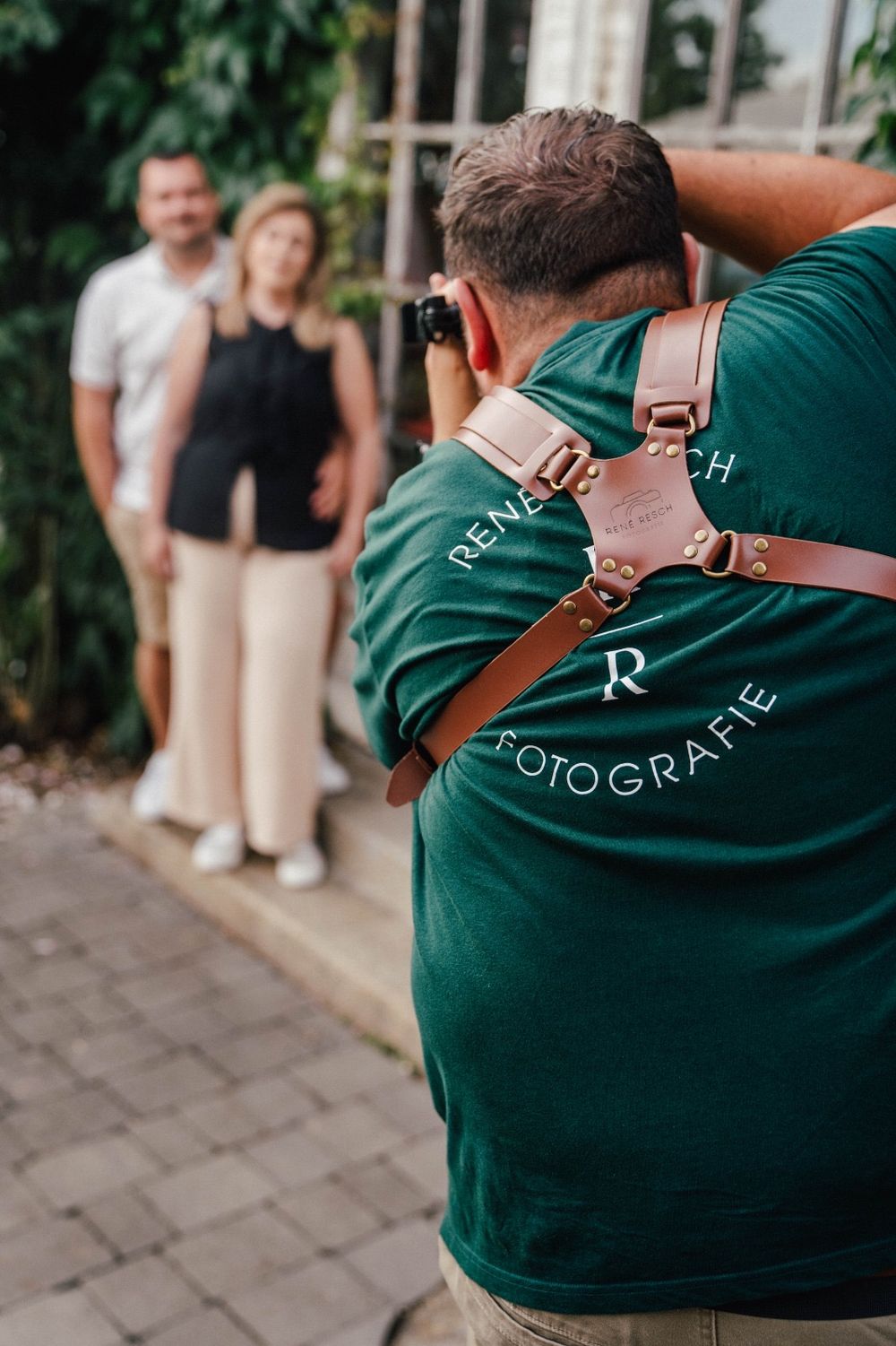 Photographer in green Fotografie t-shirt with leather camera strap photographing a couple outdoors.