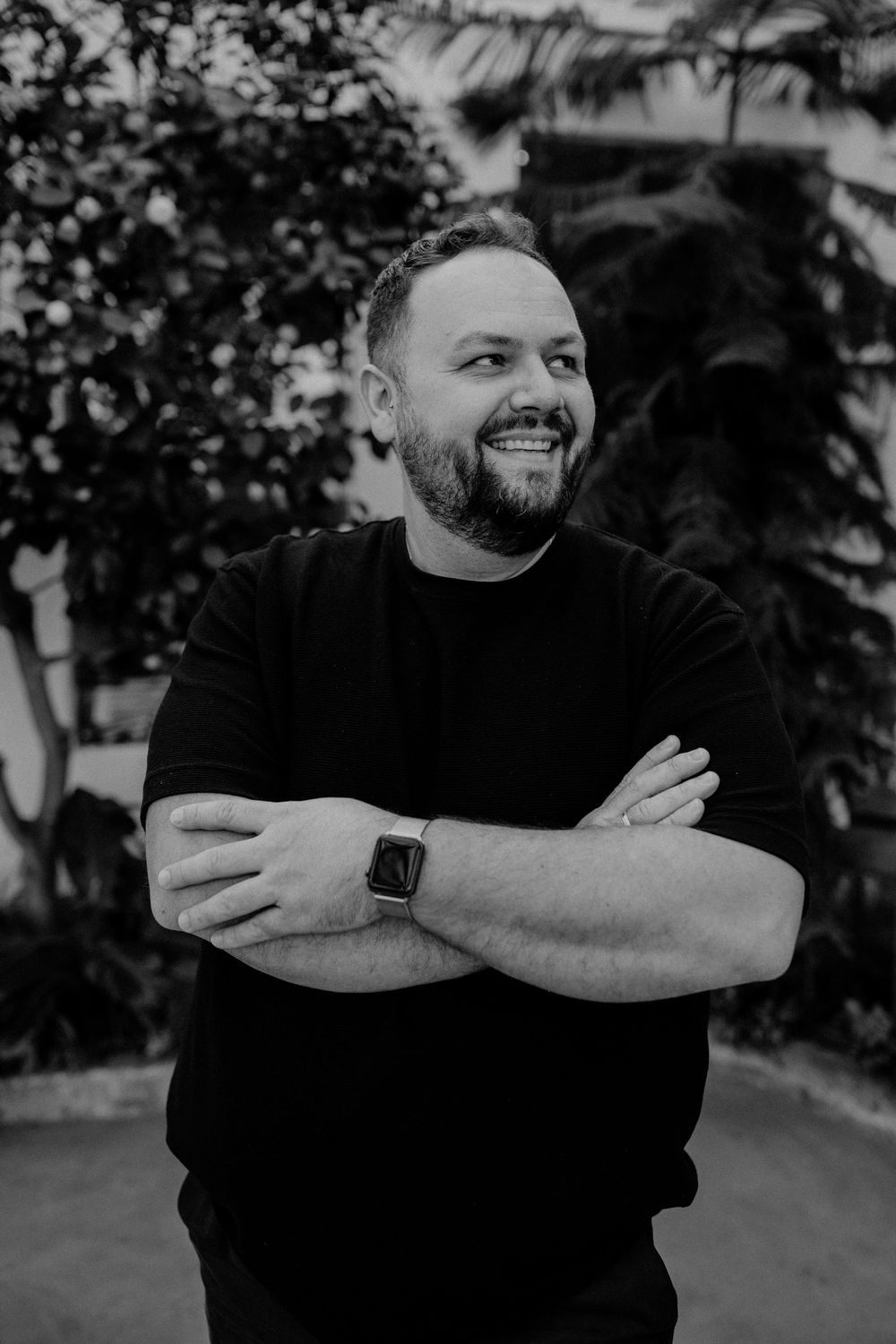 Black and white portrait of a smiling person wearing a dark sweater with arms crossed and an Apple Watch.