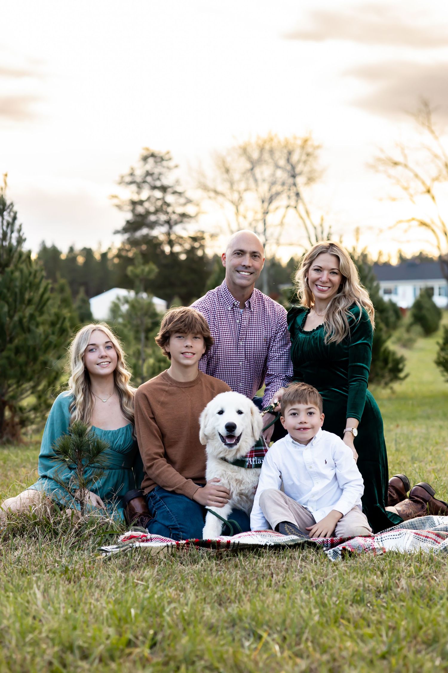 A group lies together on grass with a white dog during sunset at a family photo session outdoors. Family photographer in Richmond, Virginia