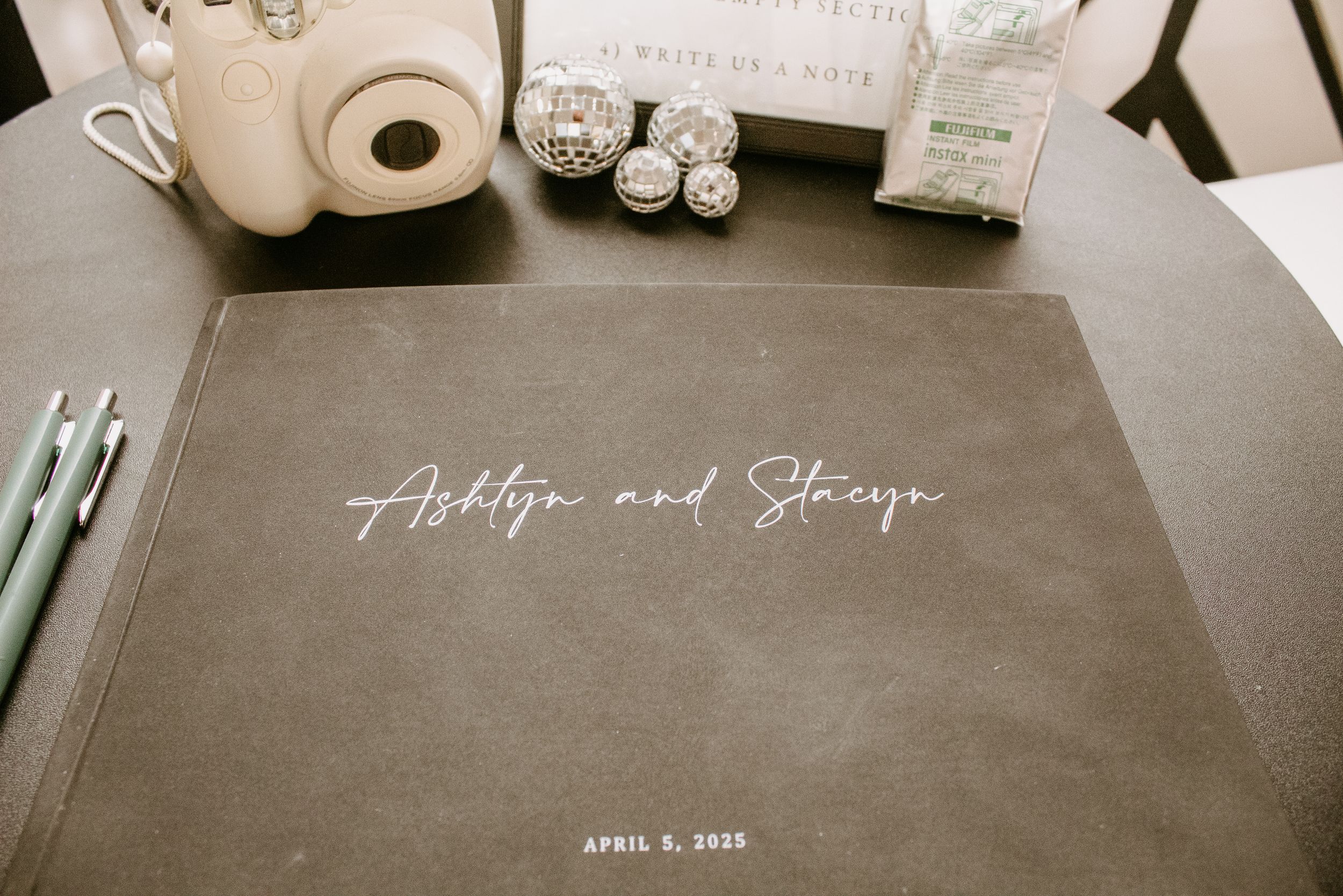 Custom wedding guest book for Ashlyn and Stacey dated April 3, 2022, displayed on a table with an Instax camera.